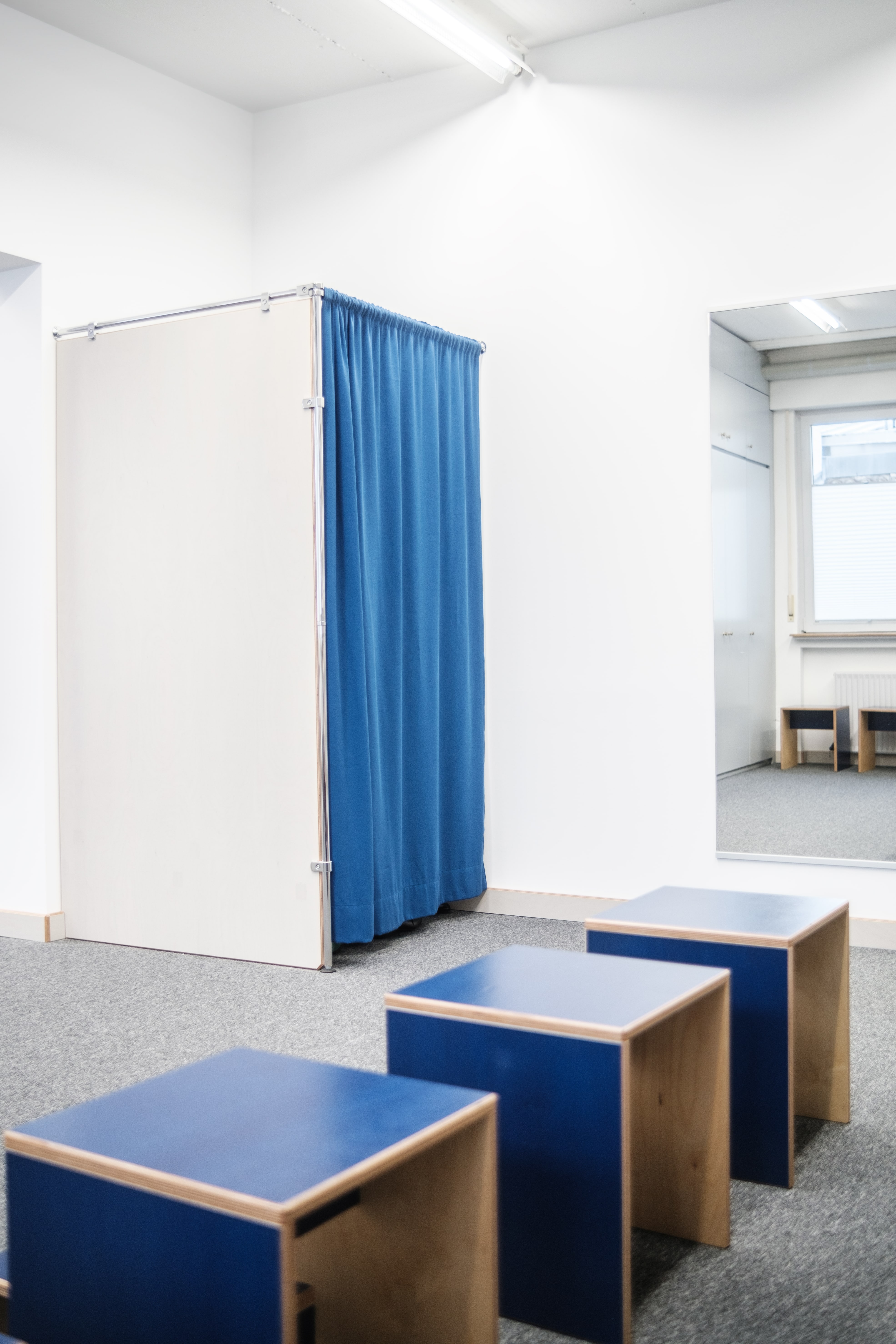 Brightly lit salesroom with fitting room featuring a blue curtain and blue stools.