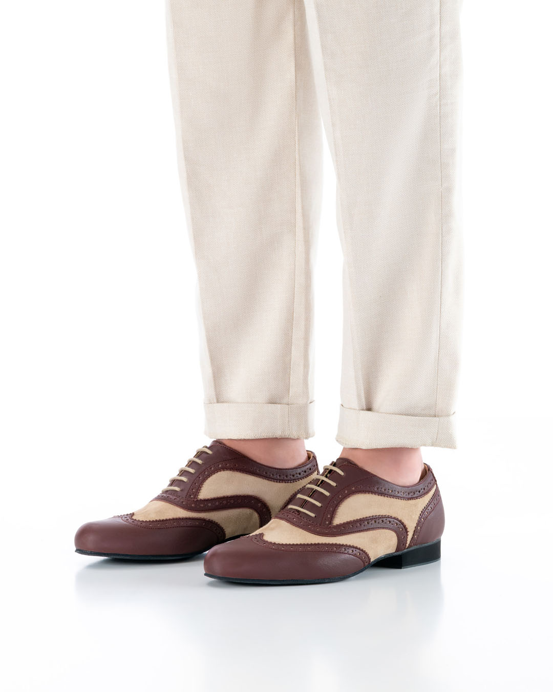 The model is standing with his feet parallel, wearing light-coloured trousers, at an angle to the camera, and is wearing elegant dancing shoes made of beige and burgundy leather with a brogue pattern and light-coloured laces
