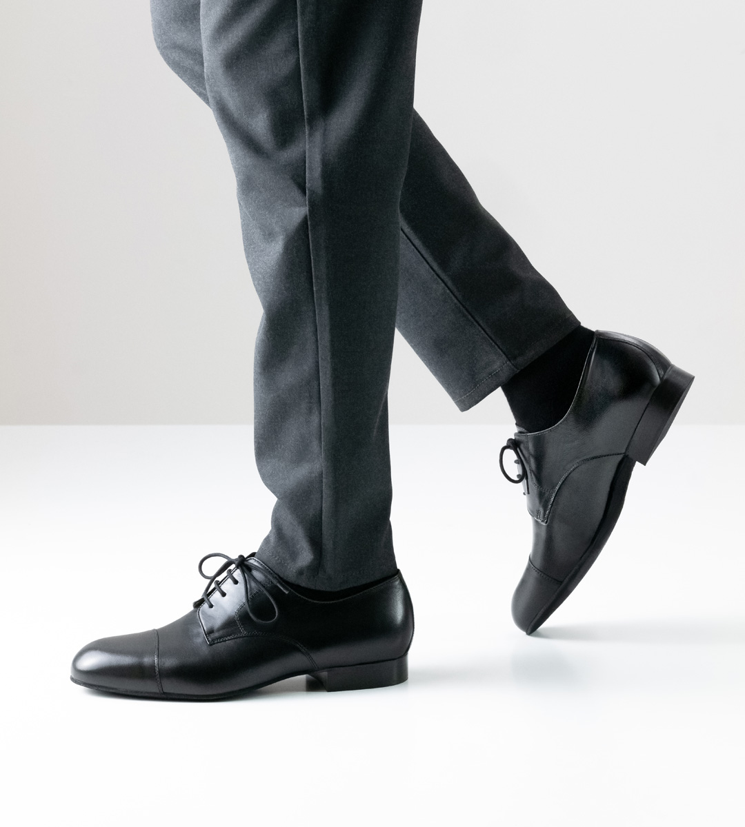Men's dance shoe in black leather with 2 cm high heel in combination with grey trousers