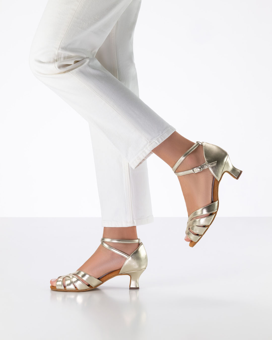 The model is standing sideways and lifting one foot backwards, wearing golden dance sandals by Anna Kern.