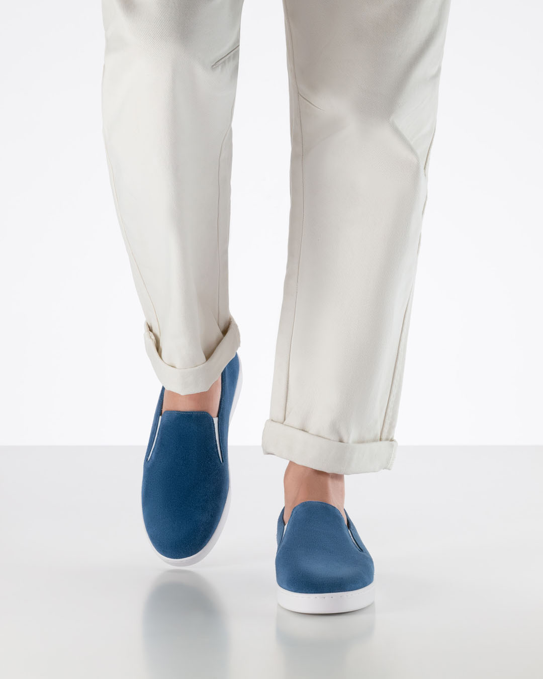 A model walks towards the camera wearing white trousers and blue suede dance trainers with white soles