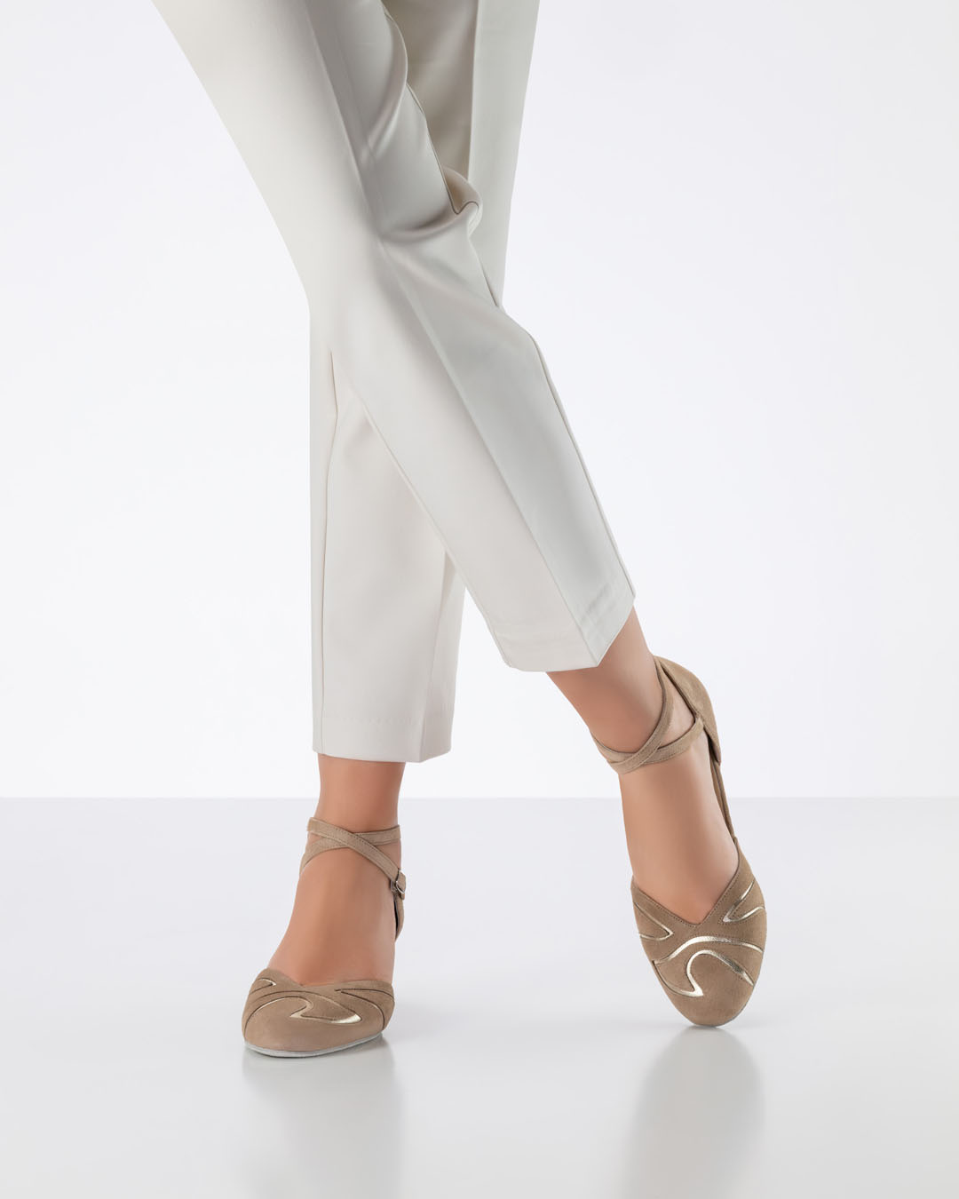 A model in light beige trousers has her legs crossed and is wearing beige, closed-toe dance shoes by Werner Kern