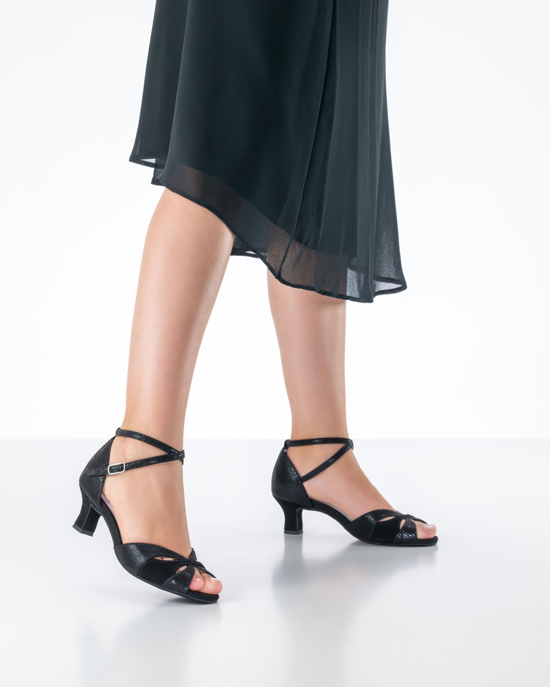 A model wearing a black chiffon dress showcases the black ‘Eunice’ dance sandals with a 5 cm flared heel by Anna Kern