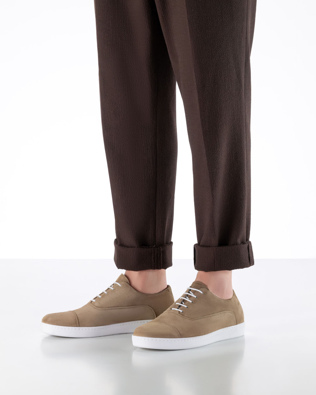 Beige men’s leather dance shoes with a white, lightweight trainers’ sole, suitable for dancing indoors and outdoors, paired with brown fabric trousers