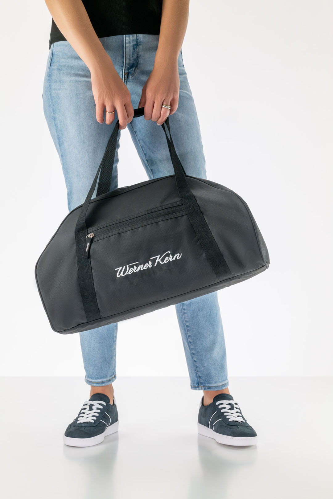 A Werner Kern sports bag in black with white logo lettering, worn by a model with jeans