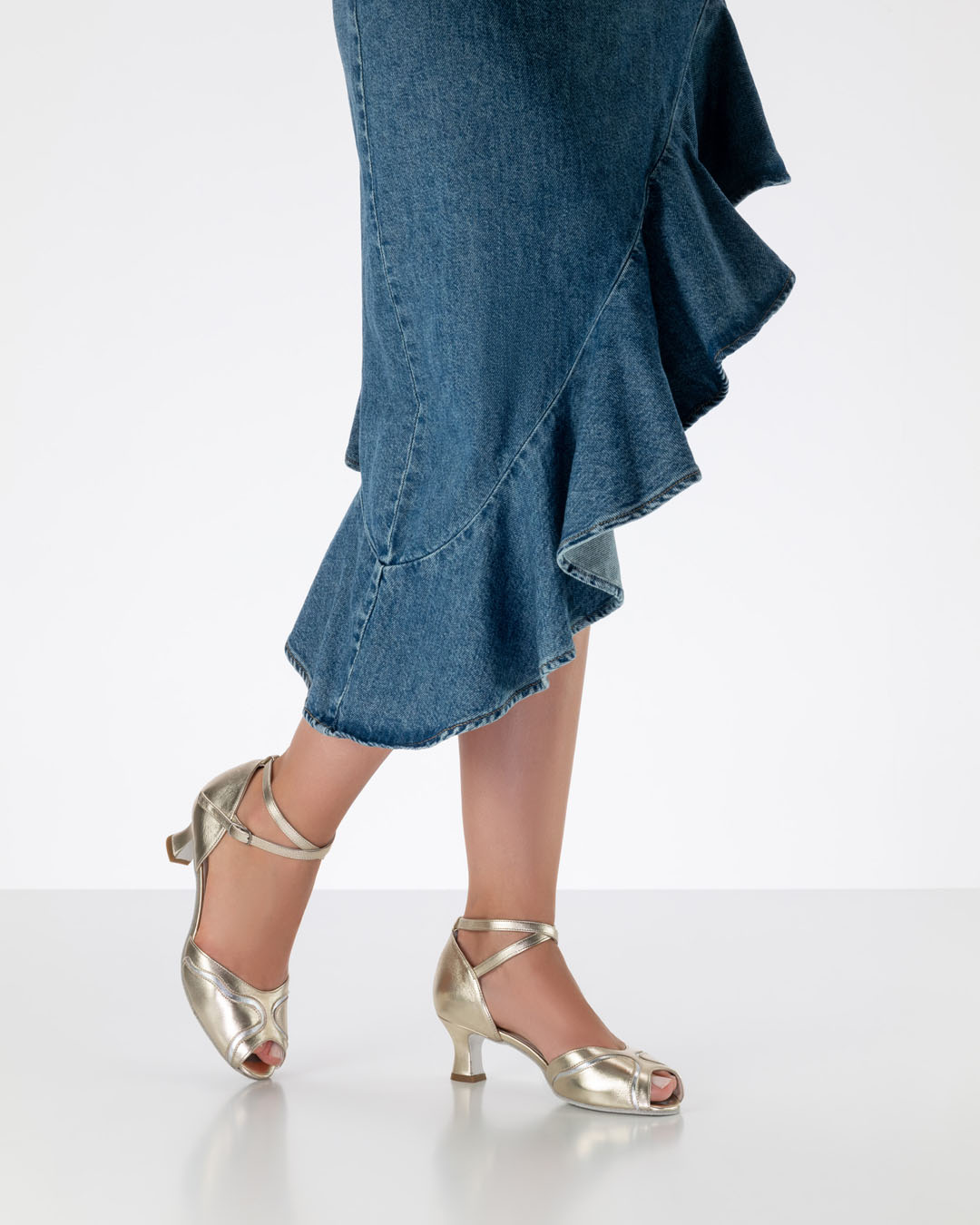A model in a ruffled skirt is wearing gold dance sandals with silver detailing