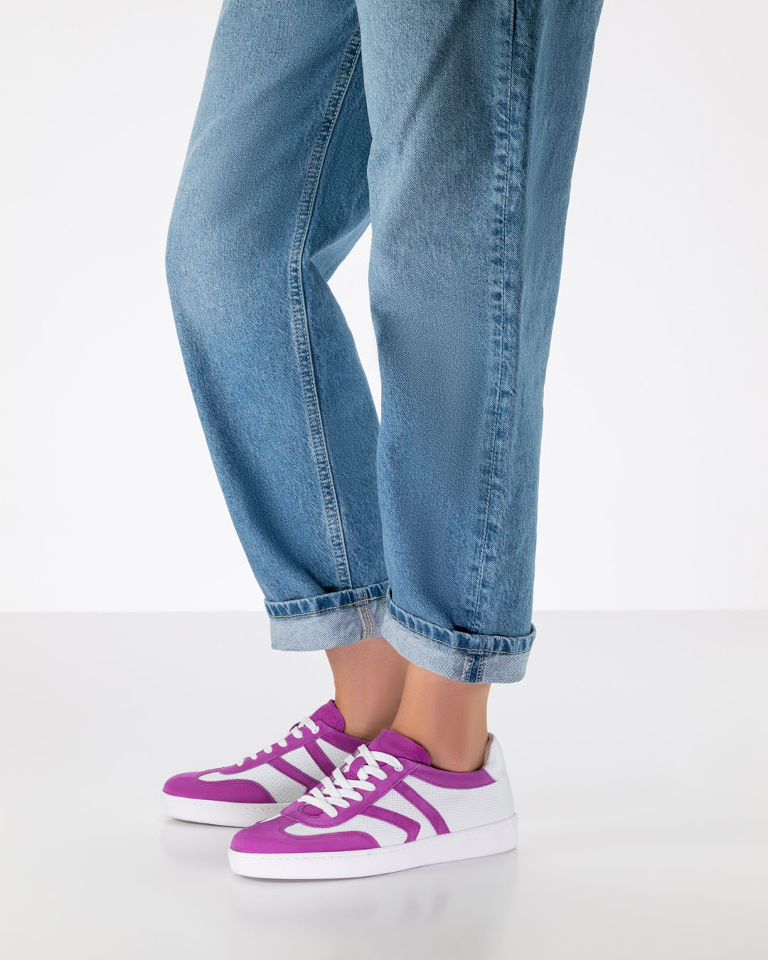 The legs of a dance shoe model wearing loose-fitting jeans and dance trainers made of white and pink leather with a white PU sole