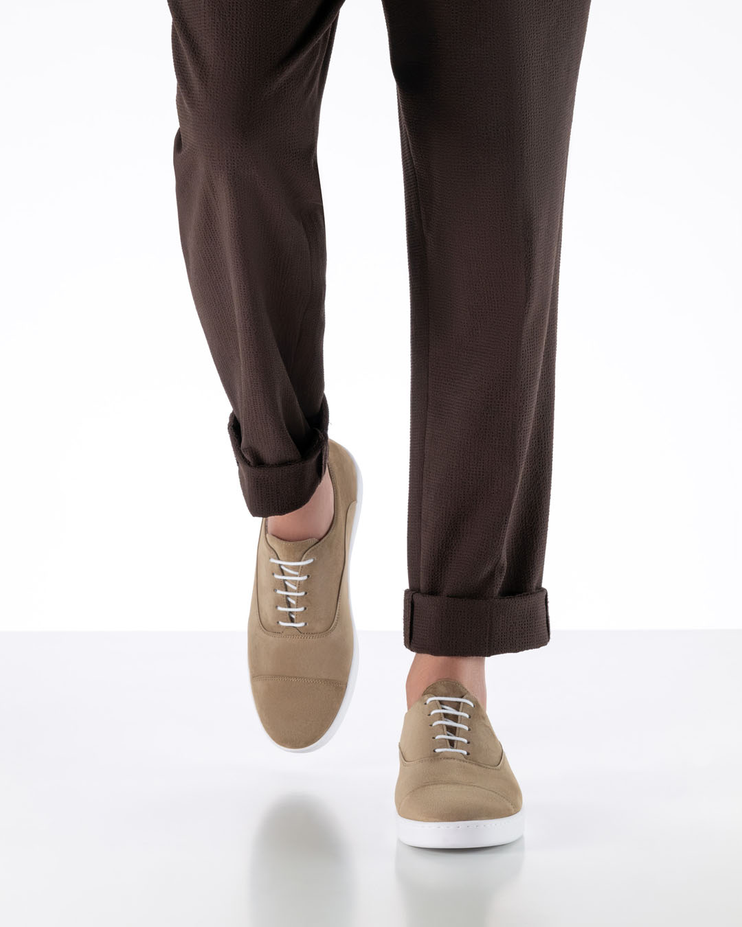 The model walks towards the camera, wearing light beige dance shoes with a white, flat trainer sole